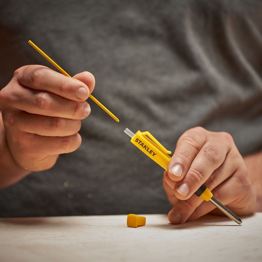 Person holding a STANLEY yellow circuit tester screwdriver and probe on a table.