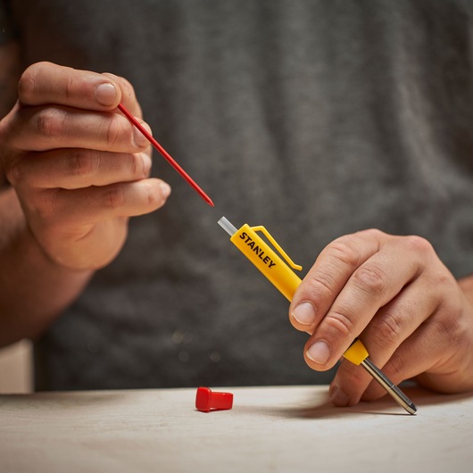 Hand holding STANLEY voltage tester screwdriver, inserting red probe, cap on table.