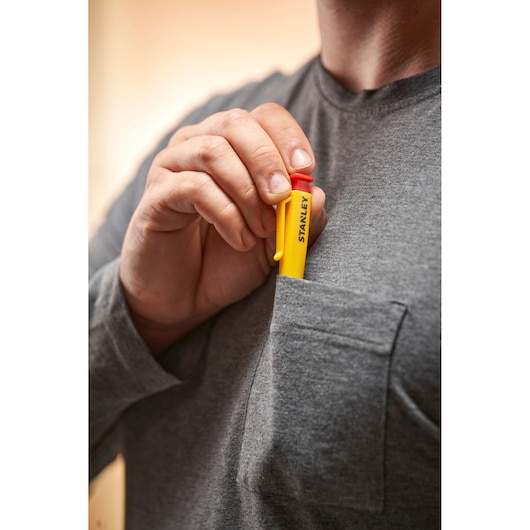 Hand placing a yellow Stanley photography tool in a gray shirt pocket.