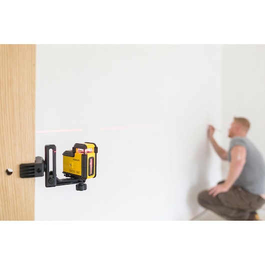 STANLEY STHT77504-1 laser level device mounted on wood, emitting red line, person marking wall.