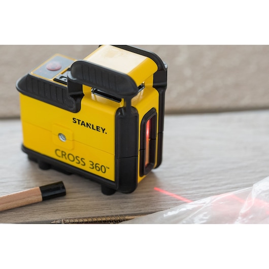 STANLEY STHT77504-1 Cross 360™ yellow laser level on tabletop, side angle, red beam visible.