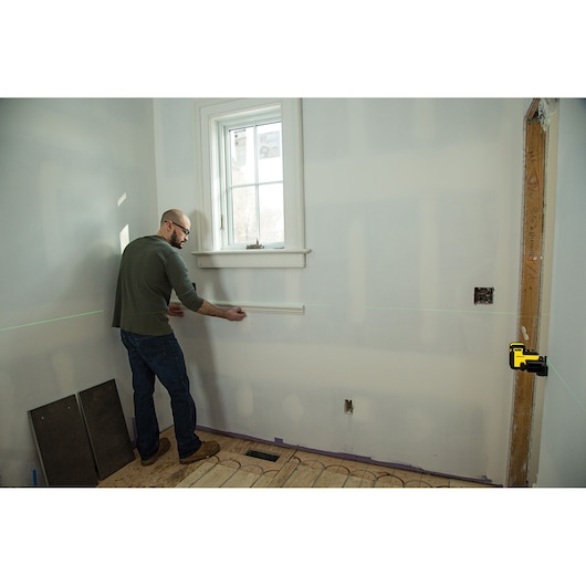 Photo of STANLEY STHT77594-1 laser level projecting green line on wall, person aligning trim in room.