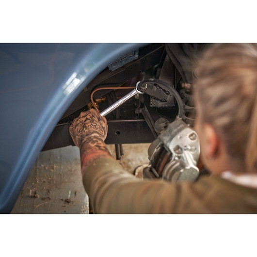 STANLEY STMT82846-0 flat ratcheting wrench used on car brake line, mechanic's tattooed arm visible.