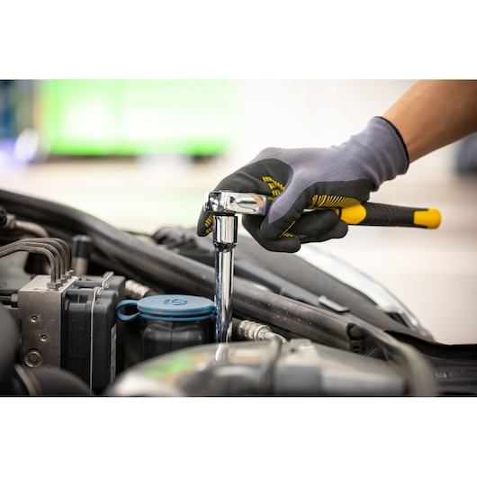 STANLEY STMT86207-0 ratchet wrench used on a car engine, close-up, with gloved hand.