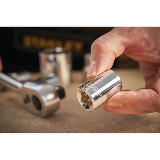Photo of STANLEY STMT86522-0 chrome socket held by hand, with ratchet and other sockets in background.