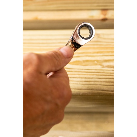 Photo of STANLEY STMT89910-0 ratcheting wrench held in hand, wood background, close-up view.
