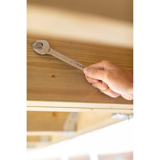 STANLEY STMT89911-0 wrench in use turning bolt on wooden beam, close-up photography.