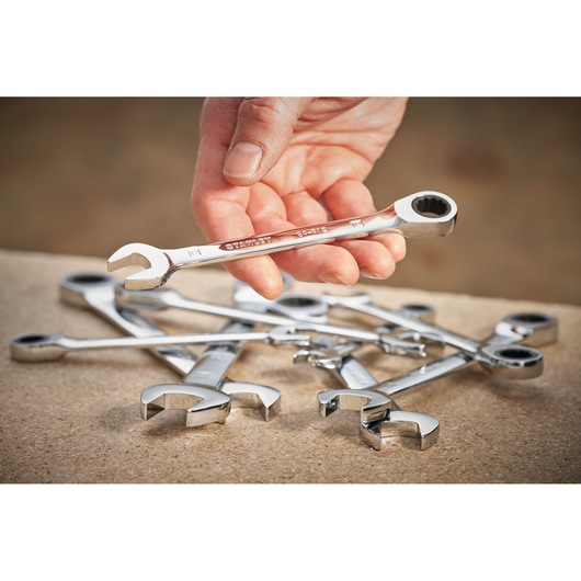 Photo of STANLEY STMT89915-0 chrome combination ratchet wrench held above matching wrenches on a work surface.