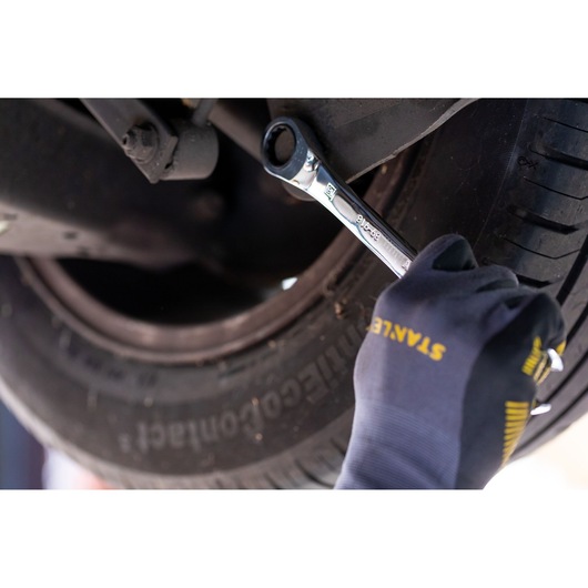 STANLEY STMT89915-0 ratcheting wrench used on car wheel, close-up with gloved hand.