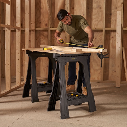 STANLEY STST1-70355 saw horses with wooden board and tools on top, used in a workshop setting.