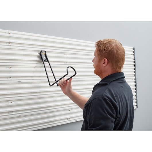 Person mounting STANLEY STST82614-1 wall hook on white wall panel system, side view.