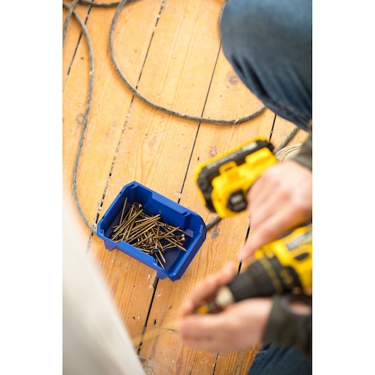 STANLEY STST82737-1 blue storage bin with screws on wooden floor, photographed from above.