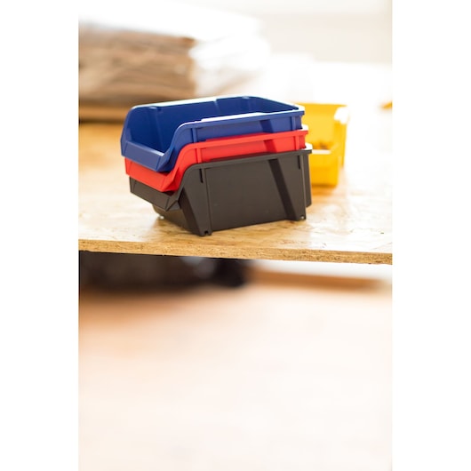 STANLEY STST82737-1 stackable plastic storage bins in black, red, blue, side angle on wooden surface.