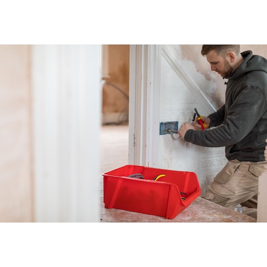 STANLEY STST82745-1 red storage bin for tools and cables in use during electrical work, side angle.