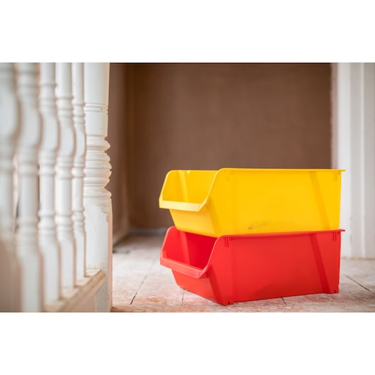 STANLEY STST82745-1 stackable storage bins in yellow and red on a wooden floor, side angle photo.