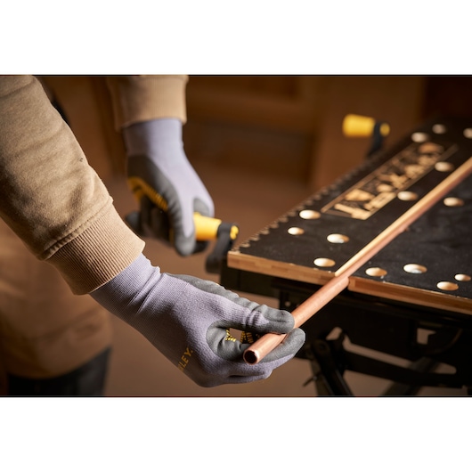 STANLEY STST83800-1 photography of gloved hands cutting copper pipe on a black workbench.