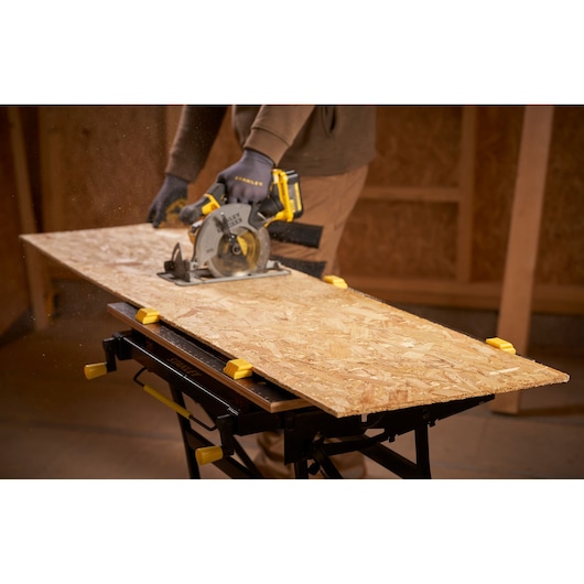 STANLEY STST83800-1 workbench in use, holding plywood with yellow clamps during sawing in a workshop.