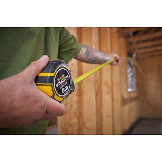 STANLEY XTHT0-33501 tape measure held in hand, yellow and black casing, measuring inside wooden framed room.