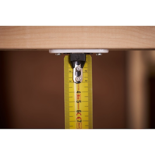 STANLEY XTHT0-33501 tape measure close-up showing yellow blade measuring under wood.